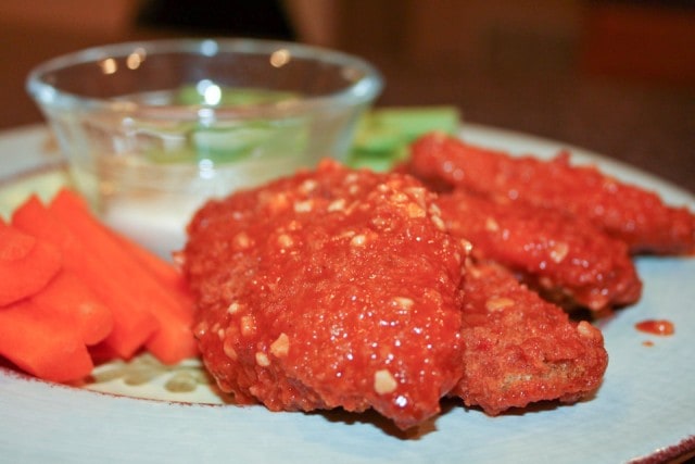 plate of boneless chicken wings covered in minced garlic and buffalo sauce with a side of carrots, celery, and dressing