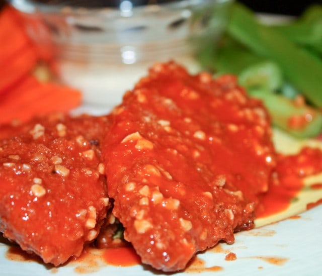 two boneless chicken wings covered in hot sauce and minced garlic with celery & carrot sticks with a side of blue cheese in the background