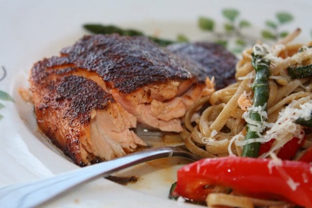 piece of broiled salmon on white plate with fork and pasta with vegetables