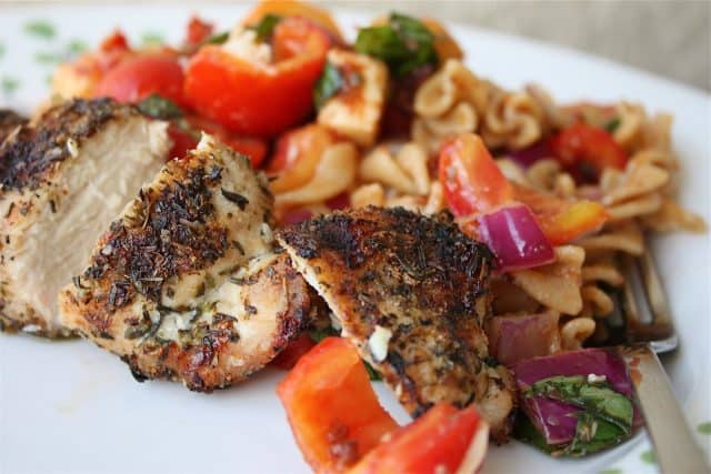 plate of herb grilled chicken with side of pasta salad with various vegetables