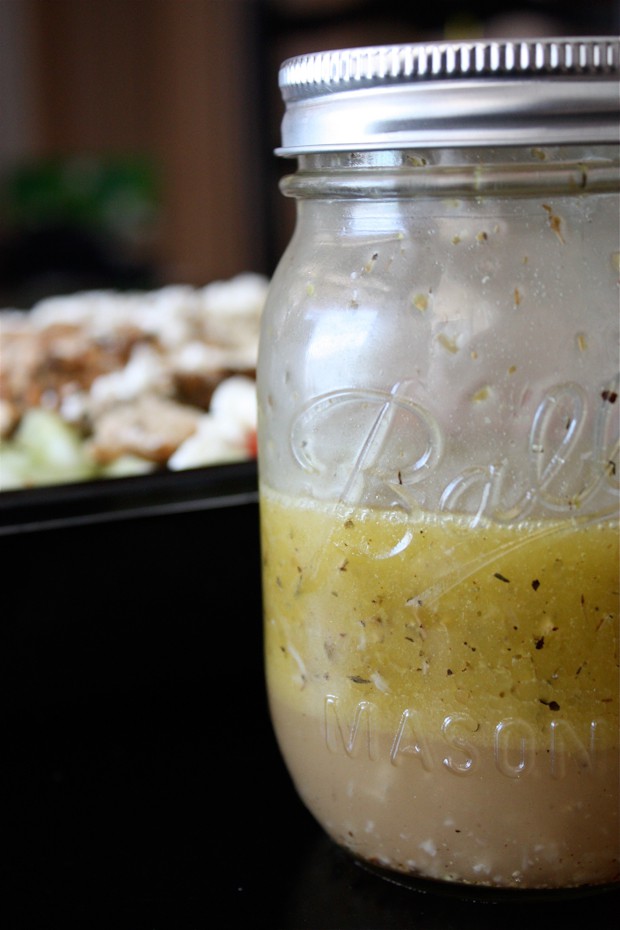 mason jar of Greek salad dressing with salad out of focus in the background
