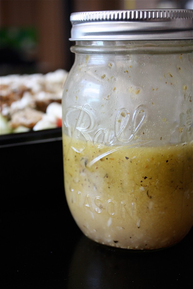 mason jar of Greek salad dressing with salad out of focus in the background
