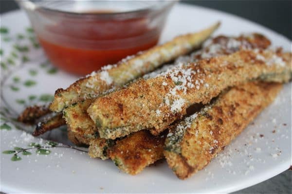 breaded and baked crispy zucchini strips on a white plate with marinara dipping sauce in background