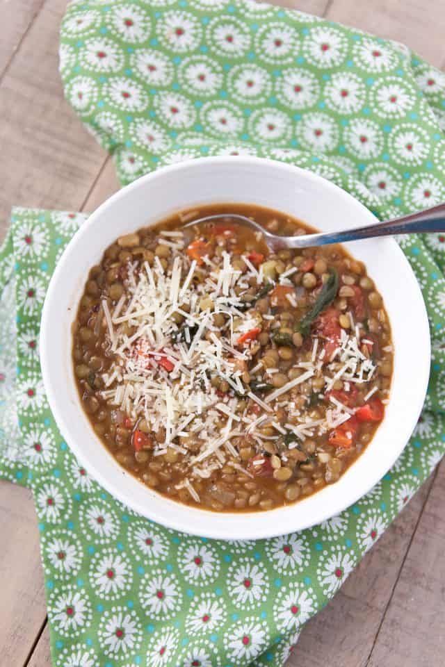 white bowl on a green napkin filled with lentil and vegetable soup sprinkled with paremsan cheese