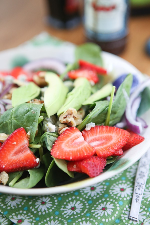 bowl of spinach salad in a bowl topped with strawberries, avocado slices, and walnuts