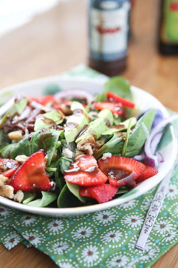 bowl of spinach salad in a bowl topped with strawberries, avocado slices, walnuts, and a raspberry balsamic vinaigrette dressing