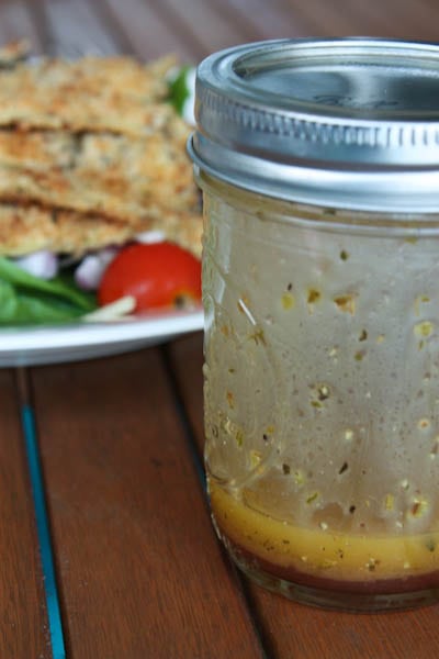 close up of mason jar with vinaigrette with salad in background