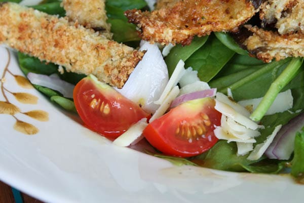 plate of spinach salad topped with cherry tomatoes, red onion, shredded cheese, and baked breaded eggplant