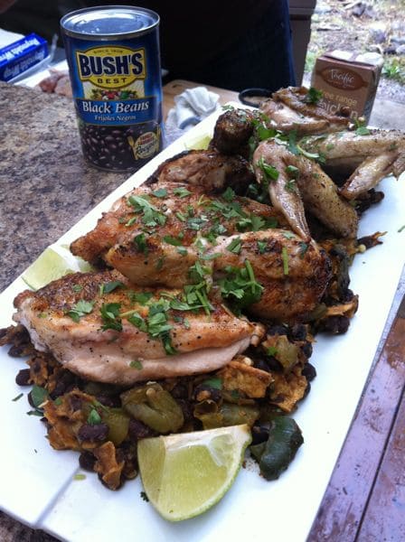 plate of grilled chicken on bed of black bean stuffing and vegetables served with a lime wedge and a can of Bush's black beans to the side