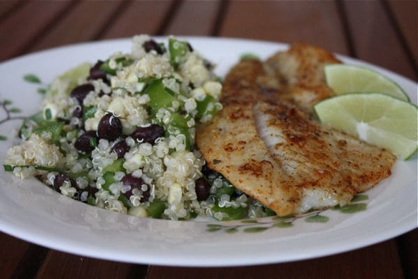 plate of cooked fish with a side of quinoa, black bean, and corn salad with two lime wedges on the side