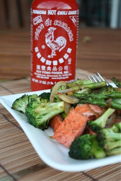 plate with the veggie and salmon stir fry with a bottle of sriracha hot sauce behind it