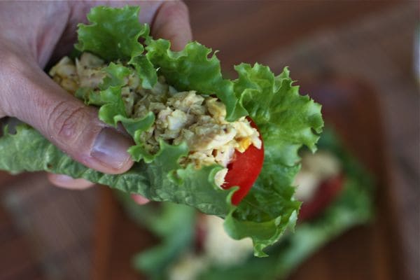 hand holding lettuce wrap stuffed with tuna salad and sliced tomato