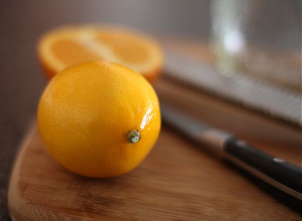whole lemon on a cutting board with half of a lemon in the background with a knife 