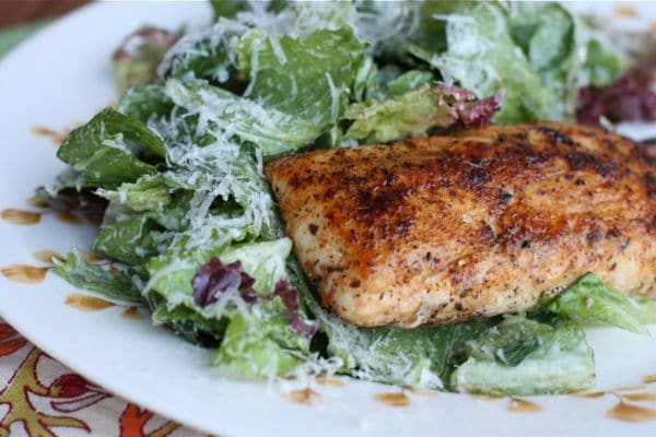 bowl of greens tossed with caesar dressing and topped with shredded parmesan cheese and blackened mahi