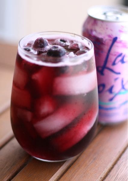 glass of wine spritzer with blueberries in front of berry la croix can