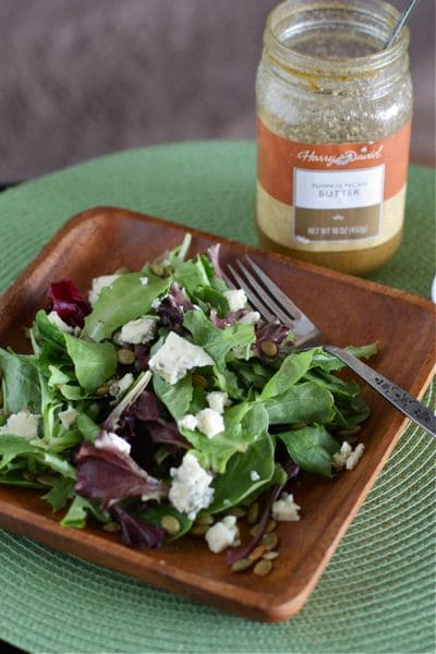 plate of mixed greens topped with pepitas and bleu cheese next to pumpkin butter vinaigrette