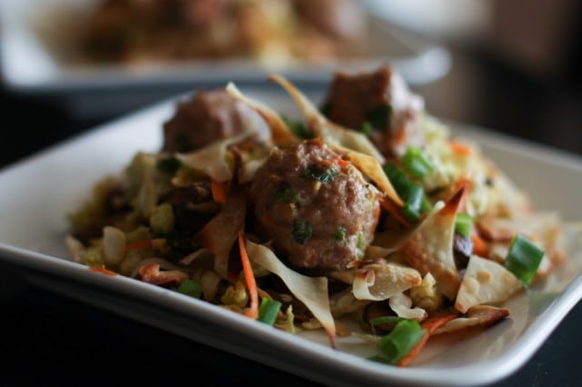 plate of chopped cabbage topped with mushrooms, carrots, green onions, wonton crisps, and meatballs 