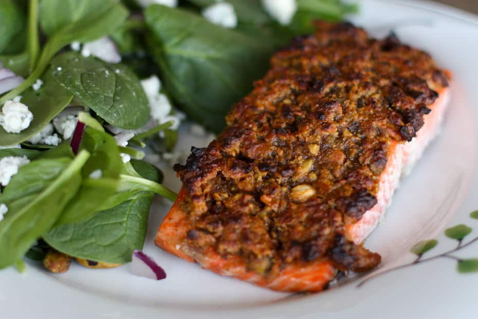 pistachio crusted salmon on white plate with spinach salad