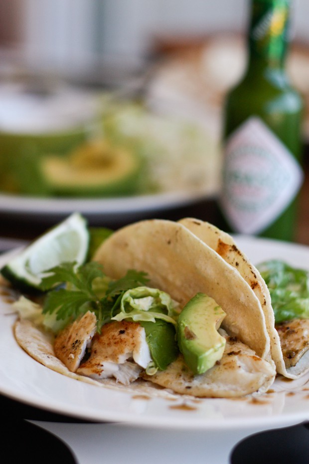 plate of two tortillas stuffed with grilled fish, fresh cilantro, and avocado with a lime wedge on the side