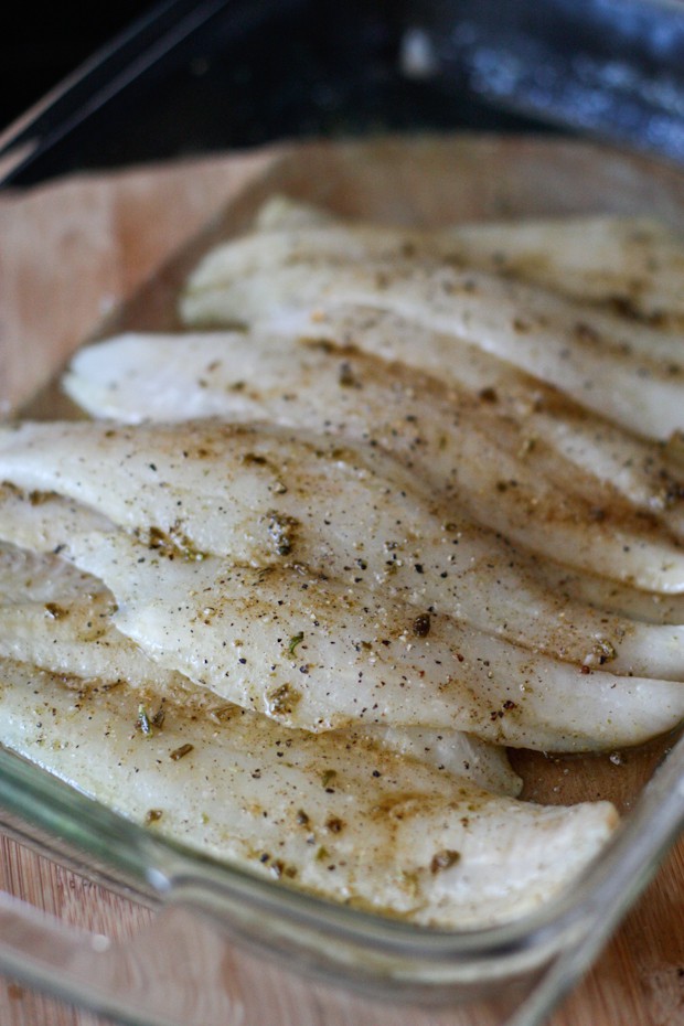 white fish in a baking dish covered with seasonings on top 