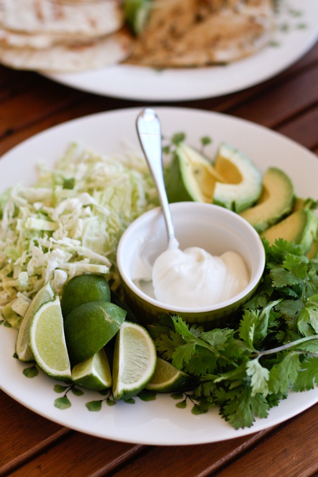 shredded lettuce, avocado slices, cilantro, lime slices, and sour cream on a plate
