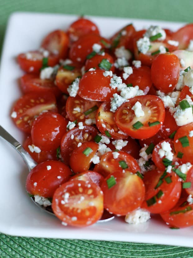 halved cherry tomatoes with chopped chives and crumbled blue cheese on a white plate
