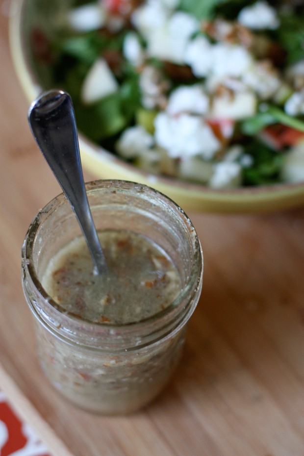 mason jar of pecan vinaigrette with spoon in it on cutting board with bowl of autumn spinach salad in background