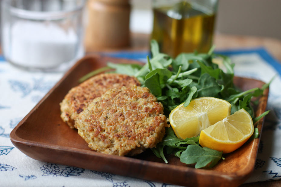 salmon quinoa cakes on a plate next to arugula salad with two lemon slices