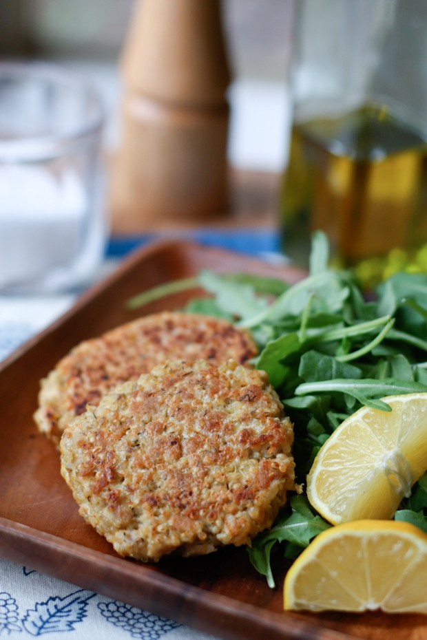 salmon quinoa cakes on a plate next to an arugula salad with two lemon slices