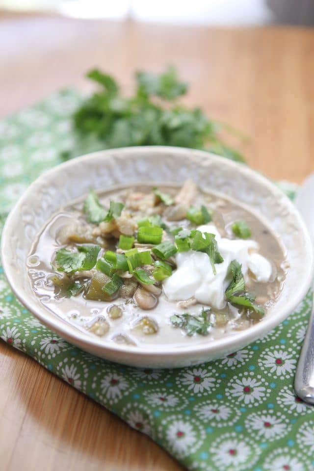 bowl of white chicken chili verde topped with cilantro, green onions, and Greek yogurt on a placemat