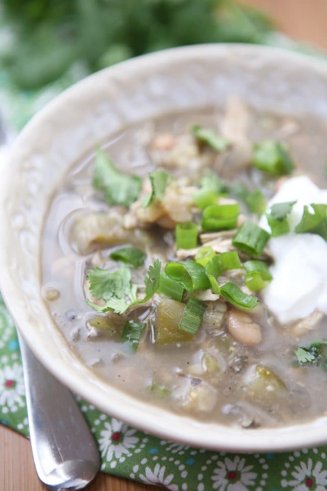 close up of bowl of white chicken chili verde topped with cilantro, green onions, and Greek yogurt