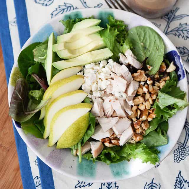 overhead photo of salad plate with greens, sliced pear, sliced avocado, chopped rotisserie chicken and walnuts