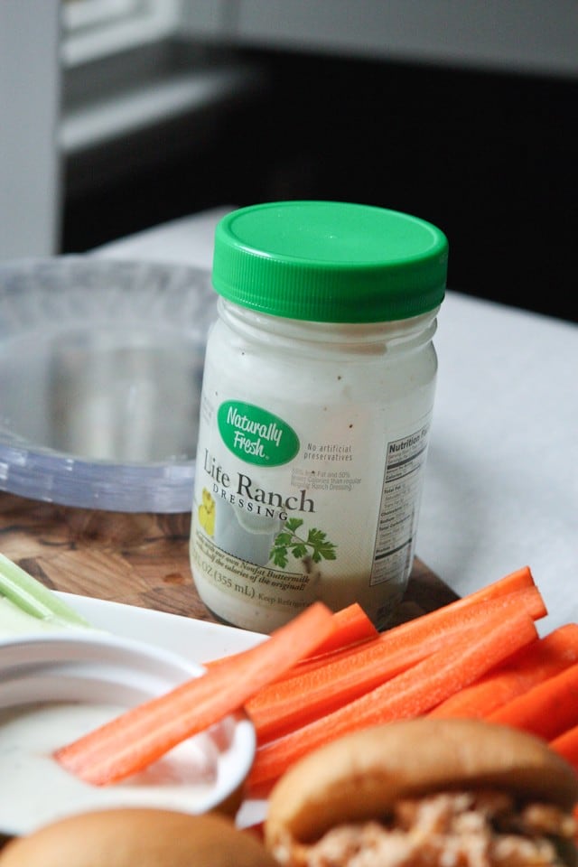 container of Naturally Fresh lite ranch dressing alongside plastic plates and carrot sticks with one carrot being dipped in a container of the ranch 