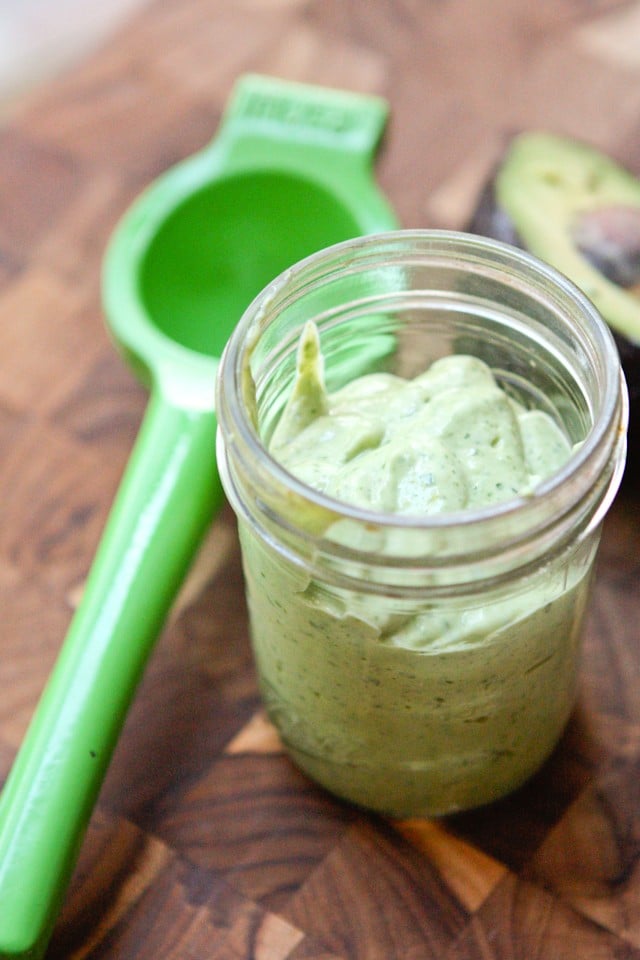 mason jar filled with creamy avocado lime dressing on a cutting board next to juicer and half of an avocado