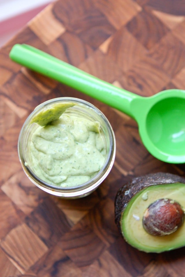 mason jar of creamy avocado lime dressing on a cutting board next to a juicer and half of an avocado 