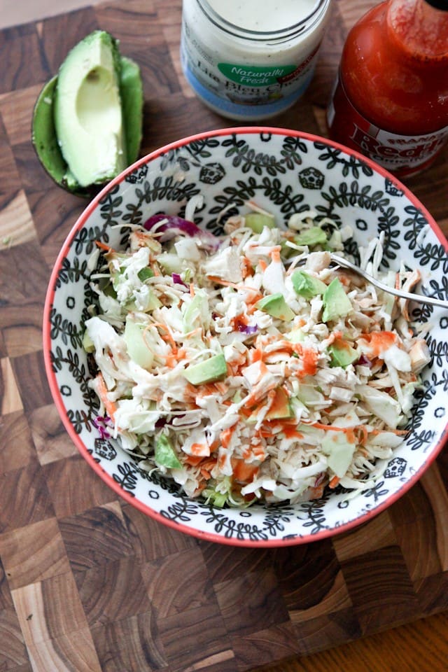 top view of bowl of chicken slaw salad topped with buffalo sauce with a container of blue cheese and buffalo hot sauce and half of an avocado