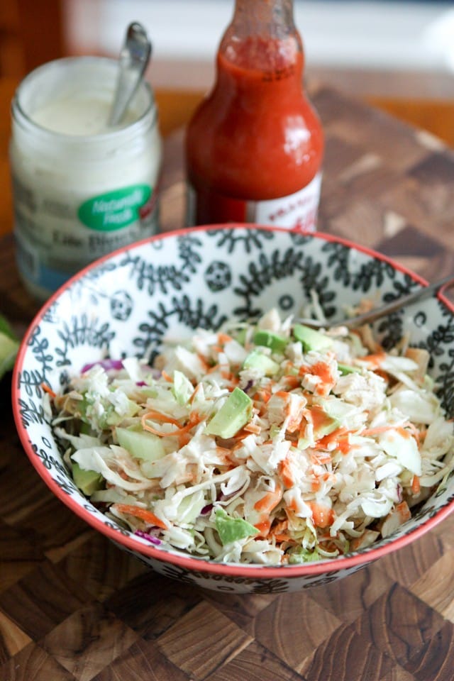 bowl of chicken slaw salad topped with buffalo sauce with containers of blue cheese and buffalo sauce in the background