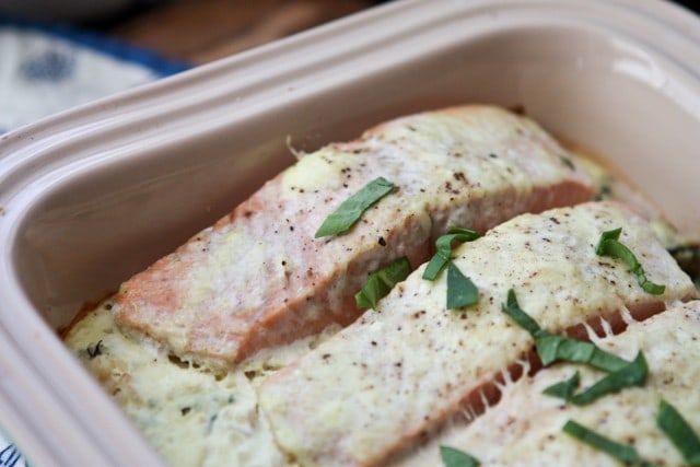 baking container with salmon topped with a creamy sauce and green garnish