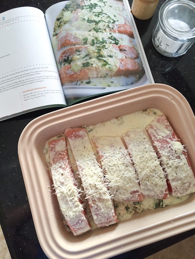 salmon spinach bake in container before going into the oven alongside Sugar-Free Mom cookbook flipped onto the recipe page