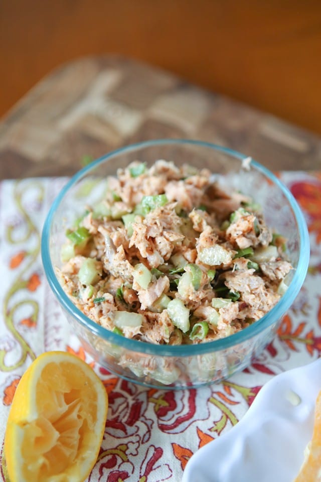 salmon salad in a glass bowl on a place mat next to half of a squeezed lemon