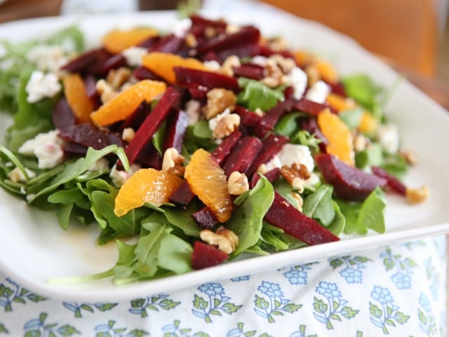 plate of arugula salad topped with goat cheese, beet strips, orange slices, and walnuts