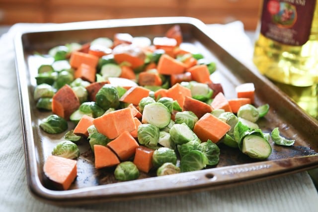 sheet pan with uncooked cubed sweet potatoes and halved brussels sprouts