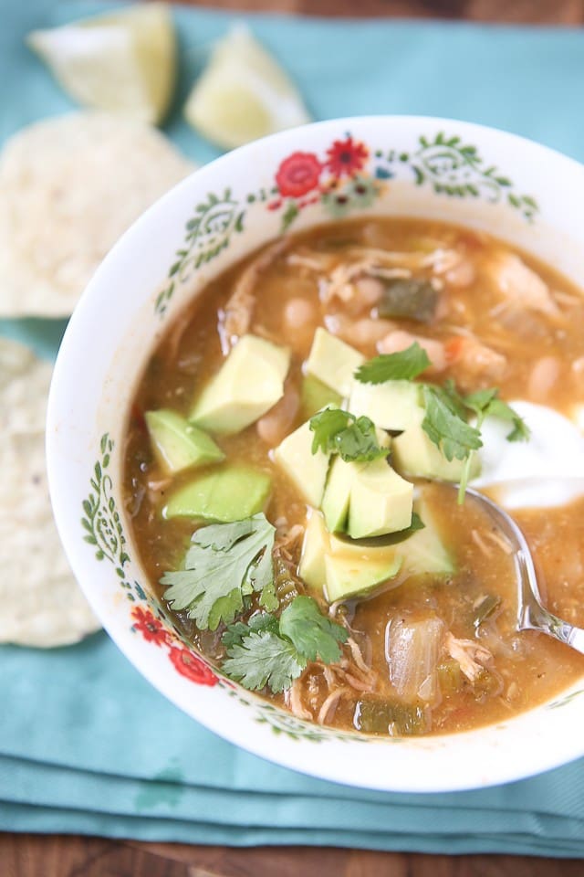 bowl of soup with shredded chicken and various vegetables topped with avocado and cilantro