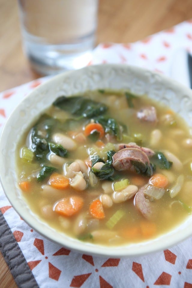 soup made with spinach beans and sausage in a cream colored bowl 