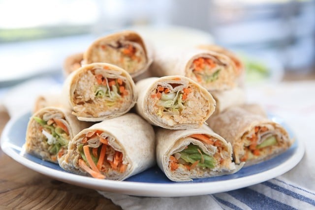 plate of wraps with various vegetables and chicken salad cut in half and stacked on each other
