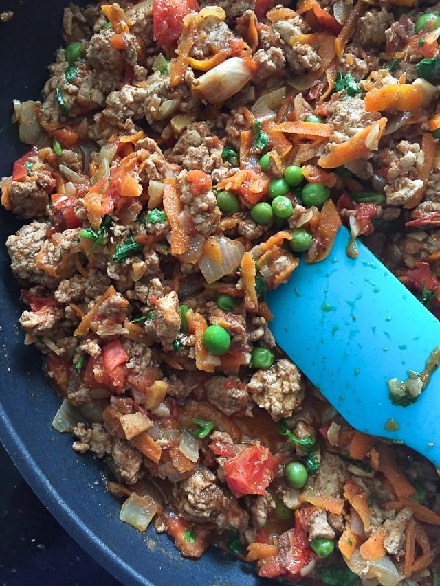 skillet of rice and ground turkey with carrots, peas, and onions with a blue spatula resting