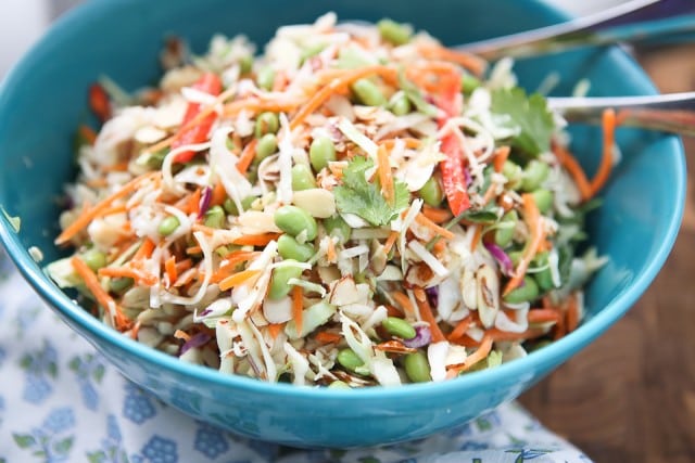 asian slaw salad of slaw mix, mathstick carrots, red bell pepper, Fisher almonds, edamame, and cilantro in a large blue bowl with utensils resting in the bowl