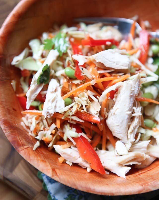 asian slaw salad of slaw mix, mathstick carrots, red bell pepper, Fisher almonds, edamame, and cilantro in a wooden bowl topped with chicken shreds