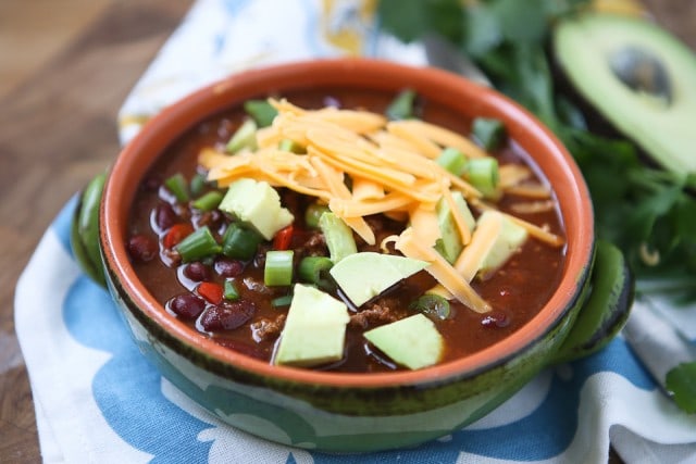 bowl of chili topped with shredded cheese, diced avocado, and scallions