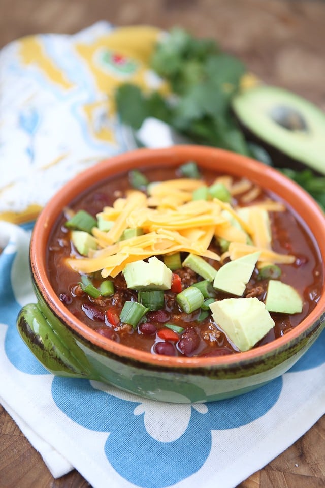 bowl of chili topped with shredded cheese, avocado, and scallions